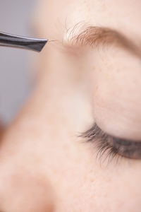 Extreme close up of young woman plucking own eyebrow hair with tweezers