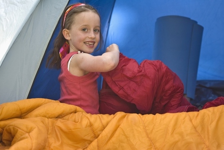 Young girl sitting inside a tent opening a sleeping bag