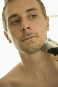 Young man shaving with electric razor