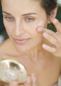 Close up of woman applying moisturizing cream and looking into mirror