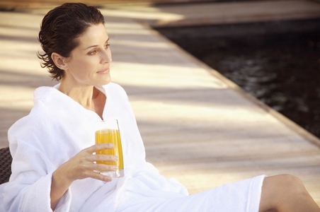 Woman sitting and drinking apple orange juice by swimming pool