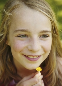 Close up of young blonde girl holding yellow flower