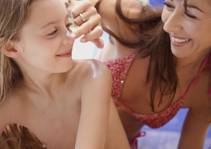 Mother applying sunscreen lotion on daughter nose
