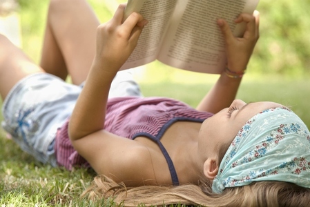 Portrait of young girl lying on back reading book