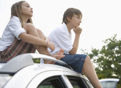 Brother and sister sitting on top of car waiting