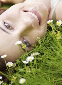Young woman laying on a field of flowers with daisy in her mouth