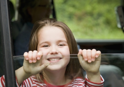 Young girl smiling with hands holding car window
