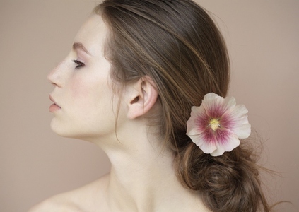 Profile of beautiful young woman with flower holding hair back