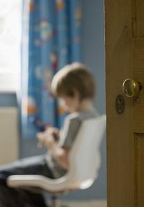 Portrait of young boy sitting text messaging on cell phone with bedroom door detail