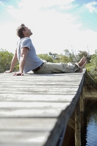Portrait of barefoot man sitting on a boardwalk by a river