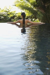 Back of young woman standing in an exotic swimming pool with arms stretched