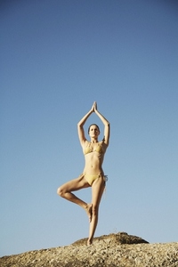 Portrait of young woman in the tree pose of yoga against blue sky