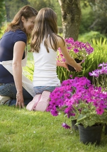 Back of mother and daughter kneeling in the garden tending plants and smiling