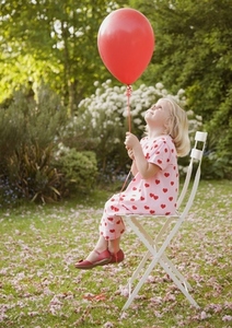 Young girl sitting on a chair in the garden holding a red balloon