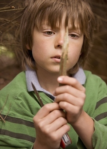 Close up of young boy sharpening a wooden stick in a campsite
