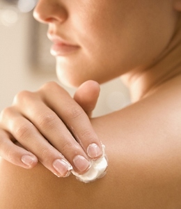 Close up of a young woman hand applying body lotion on shoulder