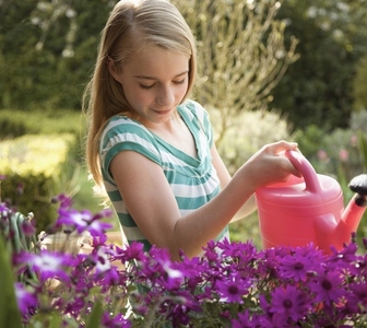 Portrait of a young girl watering flowers with pink watering can