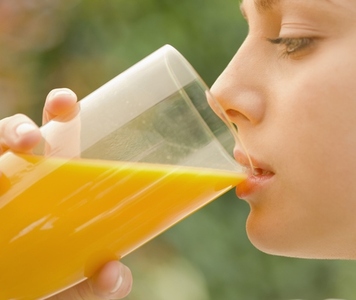 Close up of a young woman drinking and holding a glass of orange juice   profile