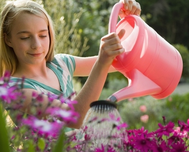 Portrait of a young girl watering flowers with pink watering can