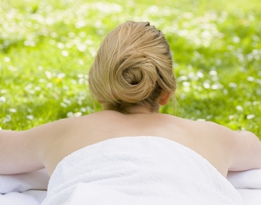 Back view of woman lying on stomach on the grass wrapped in a towel