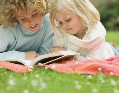 Two children lying in the garden reading a book
