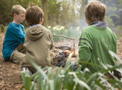 Three boys sitting around campfire cooking fish