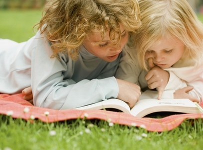 Two children lying in the garden reading a book