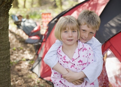Portrait of boy and girl embracing outside tent at campsite
