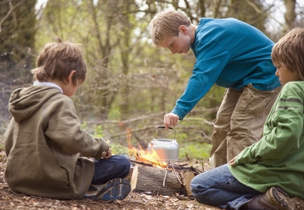 Three boys around campfire boiling water in a kettle
