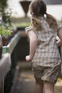 Back of young girl running around inside a nursery greenhouse