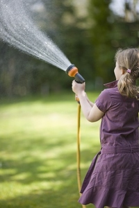 Back of young girl spraying the lawn with garden hose