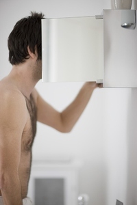 Shirtless young man looking inside a bathroom cabinet