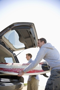 Two young men unloading surfboards from car boot