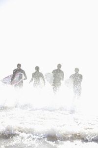 Back view of surfers running in the sea holding surfboards