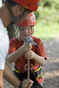 Young boy holding onto climbing rope with man helping her