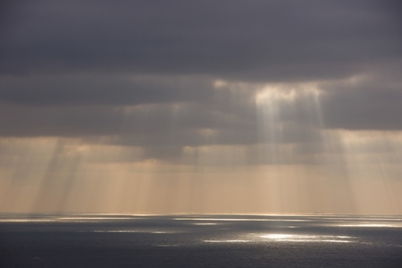 Grey sky with sun rays shining on the ocean