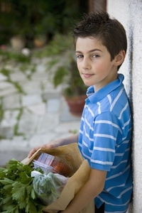 Young boy holding a brown paper bag full of fruit and vegetables