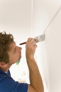 Close up of man painting under ceiling molding with a paint brush
