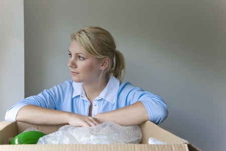 Close up of a young woman with arms resting on a cardboard box looking out