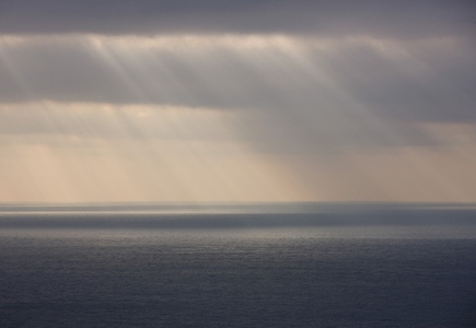 Grey sky with rain and sun rays shining on the ocean