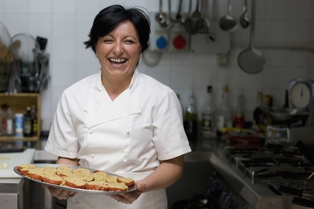 Woman chef holding a tray of stuffed tomatoes and smiling