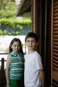 Young boy and young girl standing by window with wooden shutters