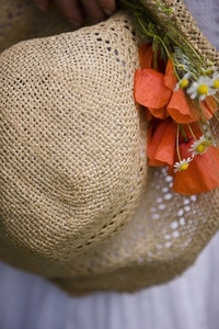 Extreme close up of a straw hat with red poppies and camomile flowers