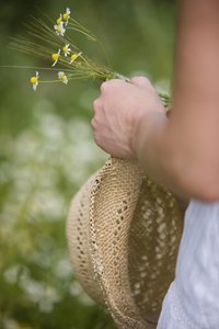 Close up of a woman hand holding a straw hat and camomile flowers