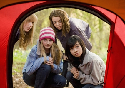 Teenage girls at campsite crouching in front of tent entrance looking in with curiosity