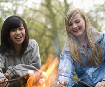 Two smiling teenaged girls roasting marshmallow over a campfire