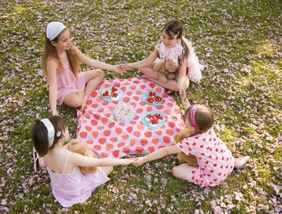 Four young girl sitting around a colorful blanket holding hands and having a party