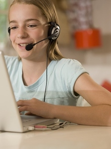Smiling young girl wearing earphones and microphone sitting at desk typing on a laptop computer