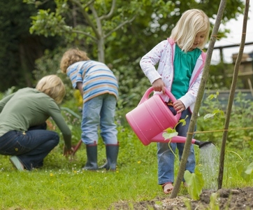 Young blonde girl standing and watering plants with pink watering can