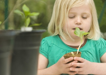 Close up of a young blonde girl inhaling and holding a seedling pot